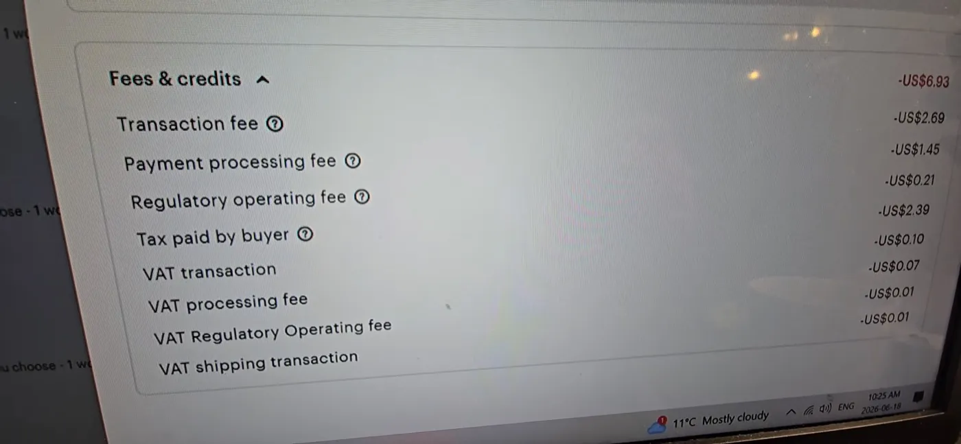 An Etsy order's Fees and credits list on a laptop screen filmed with a phone, showing the transaction fee, payment processing fee, regulatory operating fee, tax paid by buyer and VAT lines